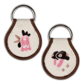 Key tags featuring embroidered designs of a bird-like figure and mushroom.