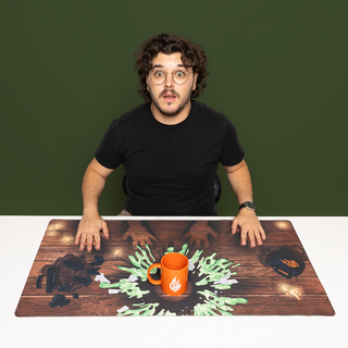 GMM Experiment Desk Mat with green splatter and an orange mug with the GMM logo on a wood-textured background.