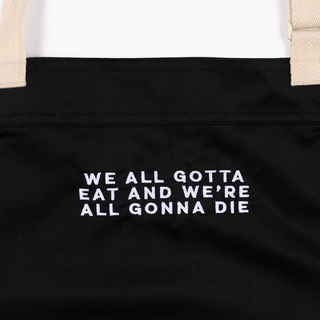 Black apron with "WE ALL GOTTA EAT AND WE'RE ALL GONNA DIE" text and a pin.