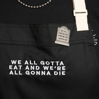 Apron and pin bundle with "We all gotta eat and we're all gonna die" text on both. Pin in tombstone shape.