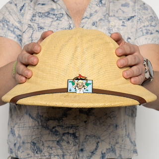 Cartographer Chase Flying Dart Pin of the Month with cartoon man in pith helmet on a map background.
